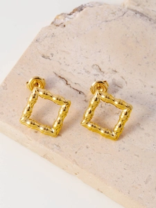 Detail showing square gold stud earrings with bamboo texture on a natural stone base