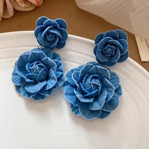 Detailed view of blue denim fabric rose flower drop earrings on a white ceramic plate
