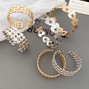 Close-up of golden hollow heart and textured woven mesh open bangles on a minimalist set