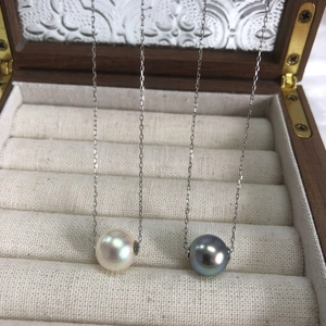 Close-up of white and black round pearls on silver chains against a jewelry box background