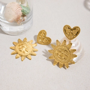 Boucles d'oreilles pendantes vintage soleil et cœur en or 18k sur fond de plage de sable blanc