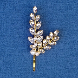Close-up of golden leaf hair clip with rhinestones and pearls on blue fabric
