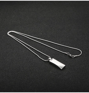 Macro detail of silver rectangular bar pendant on a sleek metal snake chain necklace