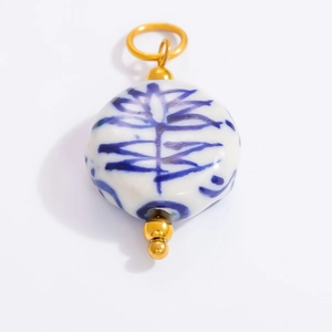 Macro shot of blue and white porcelain pendant with detailed ceramic pattern and gold bail
