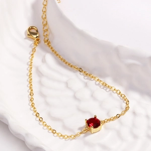 Close-up of gold chain bracelet featuring a round red gemstone and lobster clasp