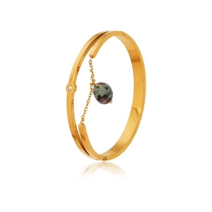 Détail du bracelet en acier inoxydable doré avec pierre verte et pendentifs en zircone