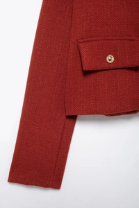 Détail d'une veste en maille rouge avec poche à rabat et bouton doré embossé