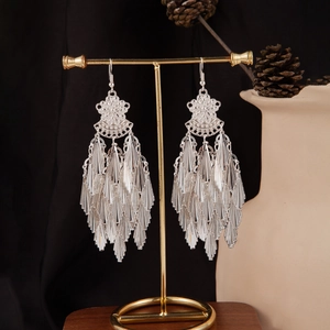 Detail of silver long tassel earrings with bohemian hollow patterns on a display stand