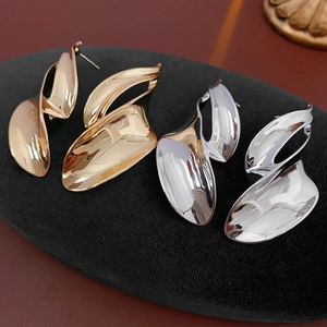 Macro view of gold and silver irregular twisted leaf earrings on a black velvet pad