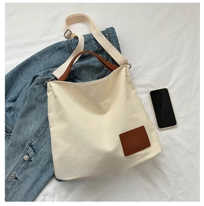 Detailed close-up of canvas tote bag with brown leather handles and brand name tag