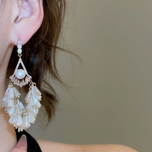 Close-up of elegant long tassel earrings with white pearls and sparkling zircons on model