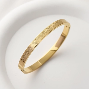 Macro shot of gold stainless steel bangle with engraved wave patterns and clasp