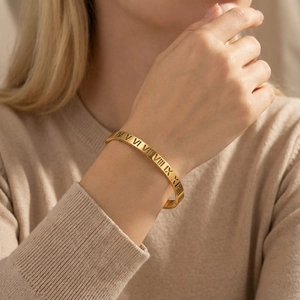 Close-up of gold titanium steel bangle with Roman numeral cut-outs on a female model