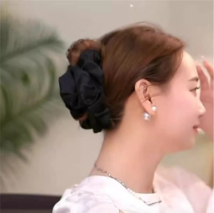 Detail of a black pleated silk-like fabric scrunchie worn on a woman's low bun hairstyle