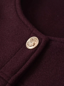 Nahaufnahme der weinroten Jacke mit geprägtem goldfarbenem Löwenkopf-Knopfdetail