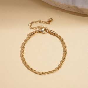 Détail d'un bracelet torsadé doré avec fermoir mousqueton sur un support beige texturé
