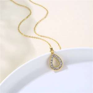 Elegant gold pear shaped necklace with white zircon crystals on white ceramic plate