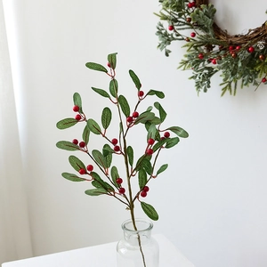 Artificial red berry branch with green leaves in a glass vase for Christmas decor