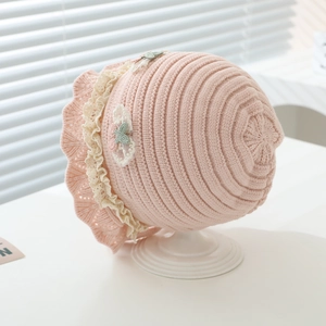 Close-up of pink knit baby hat with cream lace trim and mesh bow on white stand
