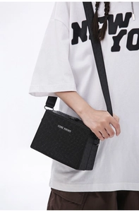 Macro shot of black ostrich-textured crossbody bag showing leather detail and metal logo