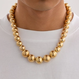 Close-up of chunky gold bead necklace worn by a male model on a plain white T-shirt