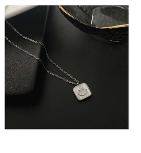 Macro detail of silver-tone titanium necklace featuring a white shell smiley face pendant