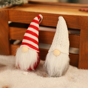 Detail of two knitted Christmas gnomes with striped and white hats on a snowy wooden background