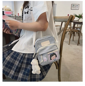 Détail du sac bandoulière en toile grise avec imprimé dessin animé et pendentif alpaga