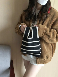 Model showing a black and white striped knit tote bag with unique top handles