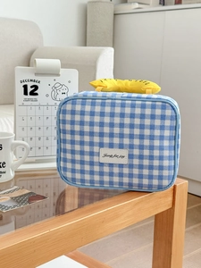 Detail der blau-weiß karierten Kosmetiktasche mit Lederetikett auf einem Holztisch