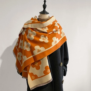 Detailed view of orange floral knit scarf with tassels paired with a black wool coat