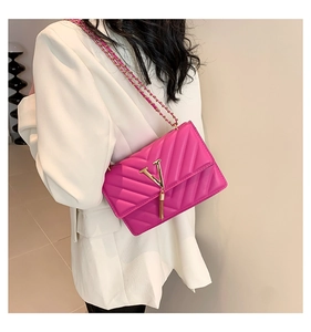 Detailansicht der fuchsiafarbenen Stepptasche mit goldenem V-Logo und Metallfransen
