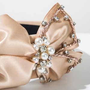 Détail d'un serre-tête en satin champagne avec perles blanches et strass brillants