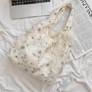 Detail of floral embroidery and lace bow on cream tote bag in a lifestyle setting