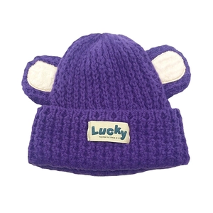 Détail d'un bonnet en tricot violet avec oreilles d'ours et étiquette Lucky bleue