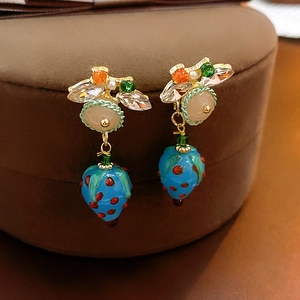 Macro view of blue strawberry earrings with colorful rhinestones on a leather box