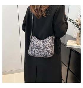 Grey leopard print crescent bag with black strap worn over a black jacket in daily scene