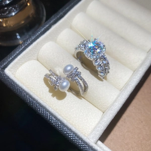 Detail of luxury zircon and white pearl rings on a beige velvet jewelry box background
