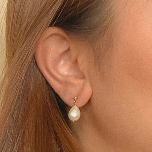 Detailed side view of water drop baroque pearl earring worn on model for scale
