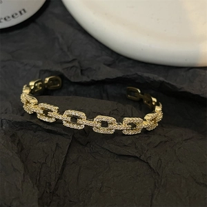 Macro detail of a gold chain style open bangle with sparkling cubic zirconia pavé