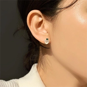 Close-up of heart-shaped shell stud earring with green zircon on woman's ear