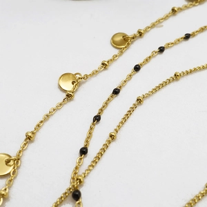 Close-up of golden multi-layer necklace featuring oval pendants and black bead accents