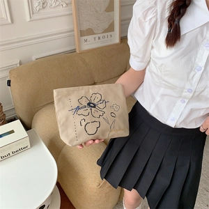 Detail of floral embroidery on canvas makeup bag held in a cozy home setting
