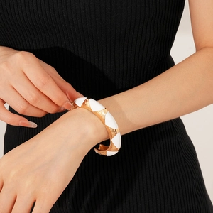 Detail of a white enamel and gold geometric bangle on a model's wrist with black attire