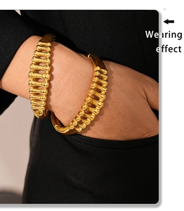 Detail showing wearing effect of gold fishbone hollow bangle on wrist with model wearing black