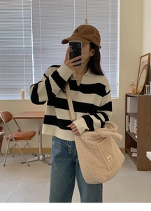 Lifestyle shot of a beige faux shearling tote bag styled with a striped polo knit sweater