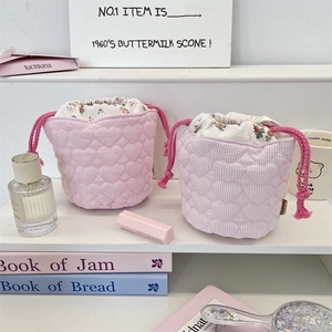 Detail of pink quilted drawstring makeup bags with heart patterns on a white shelf