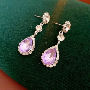 Detailed close-up of purple teardrop crystal earrings with diamond pavé on green velvet