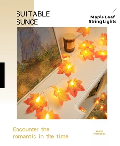 Detail of warm LED maple leaf fairy lights with realistic orange leaves on a white surface