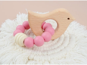 Detail of pink silicone beads and wooden bird teether on a boho macrame mat